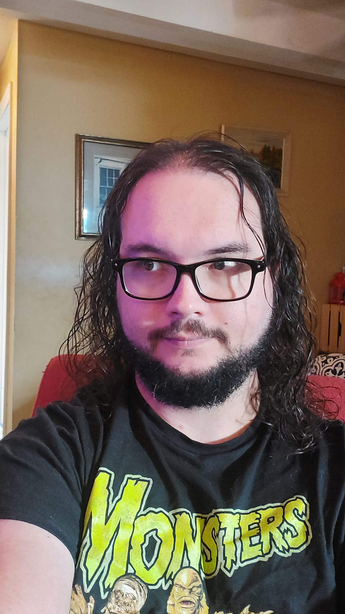 A man with long dark hair and a beard sits in a computer chair, photo 2